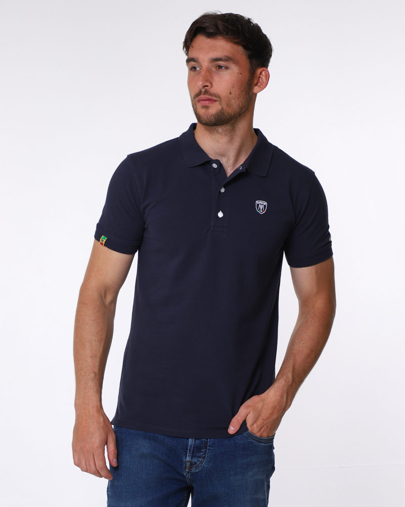 Navy blue pique cotton polo shirt, with small shield MANCINI logo on the chest and a small logo on the left arm. Contrasting black button hole stitching. The word MANCINI under the collar in black print. Red ribbon detail on the bottom inch of the t shirt on both sides.